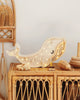 A Little Lights Whale Lamp, shaped like a whale, brightens a cozy room corner, casting warm light through patterned holes on its body, placed atop a wicker cabinet beside wooden toys and baskets.