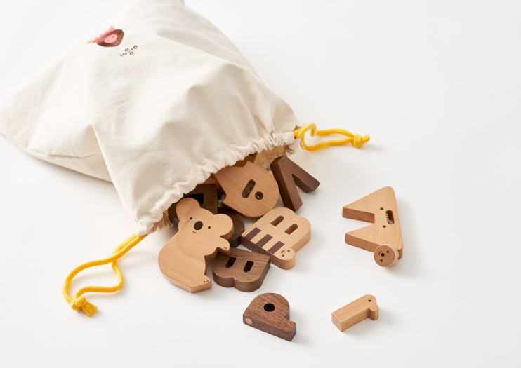 A white drawstring bag with a yellow string, spilling various Ultimate Wooden Alphabet Puzzle shapes onto a white surface.