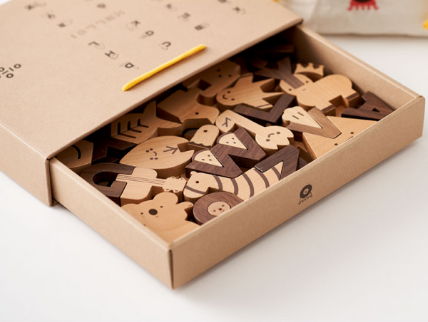 Open cardboard box filled with the Ultimate Wooden Alphabet Puzzle pieces, designed with simple, charming patterns, displayed on a white surface.