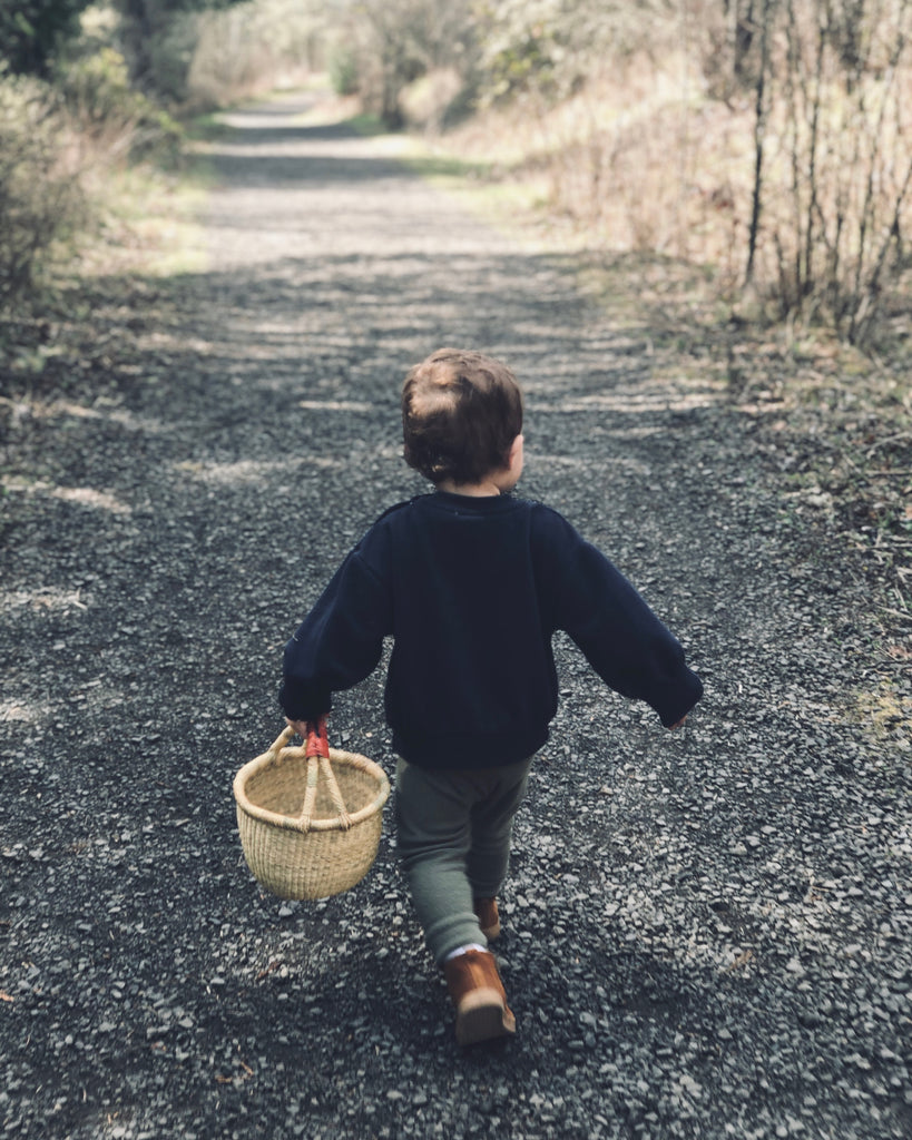 A little child holding a woven basket with a leather handle.