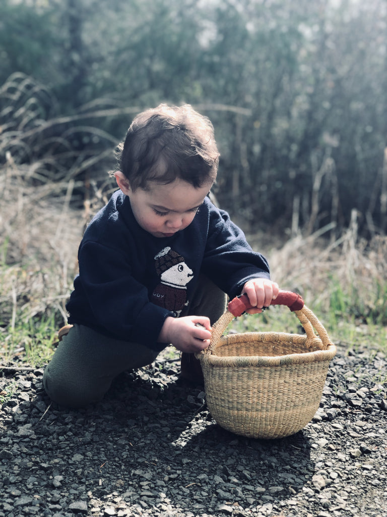 A little child holding A woven basket with a leather handle.