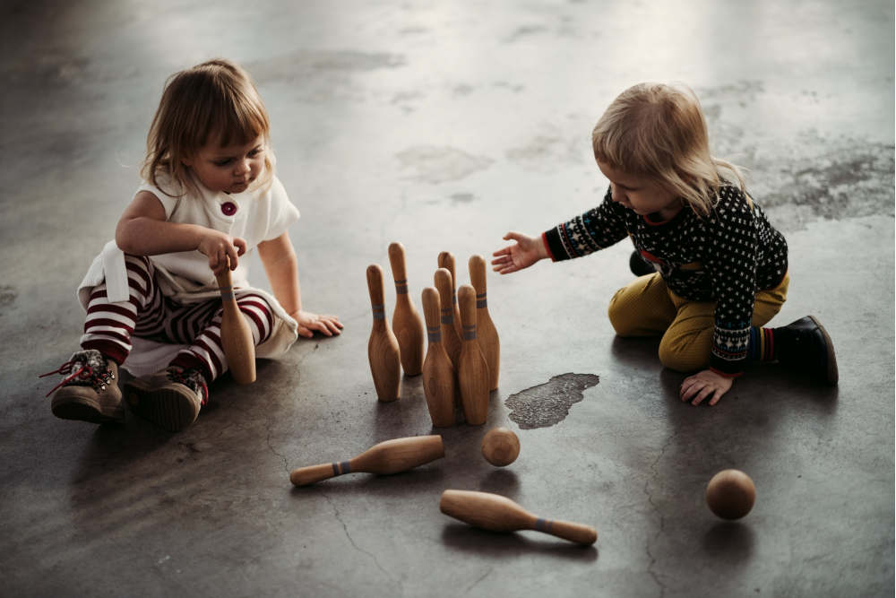 Children sitting on the floor playing with wooden bowling set. 