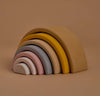 A stacking toy with 7 pastel tone wooden arcs stacked into a rainbow shape. Photographed at an angle.