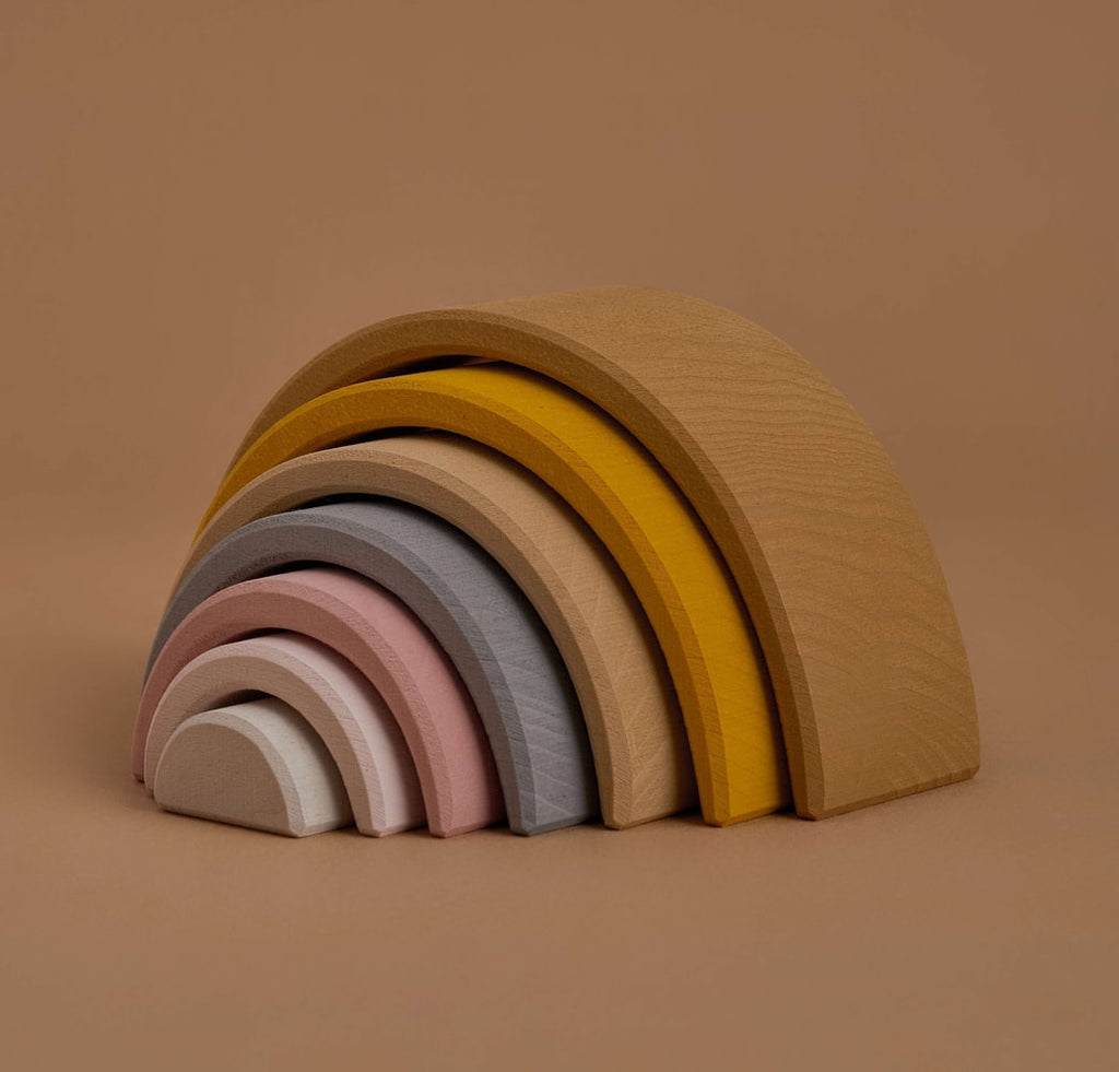 A stacking toy with 7 pastel tone wooden arcs stacked into a rainbow shape. Photographed at an angle.
