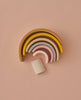 A stacking toy with 7 pastel tone wooden arcs stacked into a rainbow shape. Photographed laying on a flat surface.