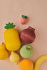 Colorful Raduga Grez handmade painted wooden fruits including an apple, banana, pomegranate, and others, arranged on a soft pink background.