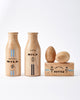 2 wooden milk bottles, 1 wooden stick of butter and 2 wooden eggs on top. White background. 