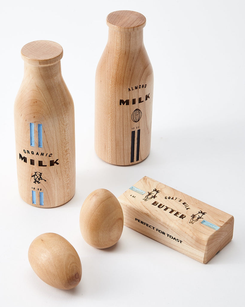2 wooden natural color milk bottles, 1 wooden natural color stick of butter and 2 wooden natural color eggs. White background. 