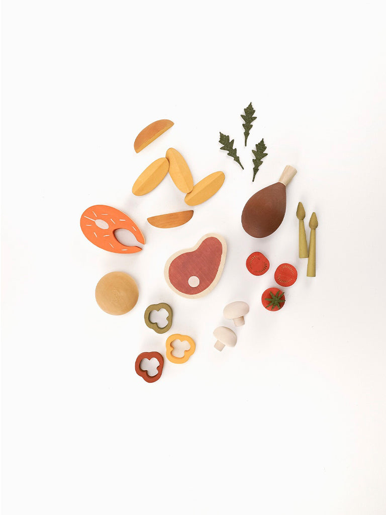 A variety of Sabo Concept Handmade Wooden Dinner Set items, including fruits, vegetables, and utensils, coated in non-toxic paint and arranged neatly on a light background.
