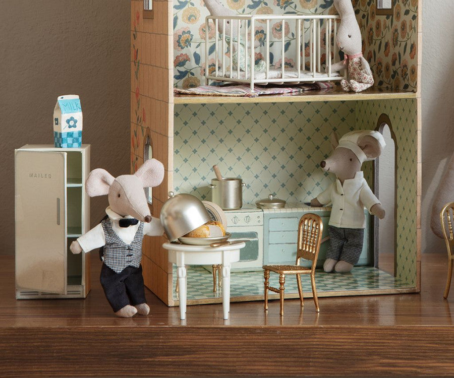 A charming miniature scene featuring two mouse figurines in a kitchen setup with a Maileg Mini Side Table, cookware, and furniture. One mouse is cooking at a stove, while the other, dressed in