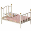 A Maileg Miniature Bed with golden knobs, adorned with a pink knitted blanket and a floral pillow.