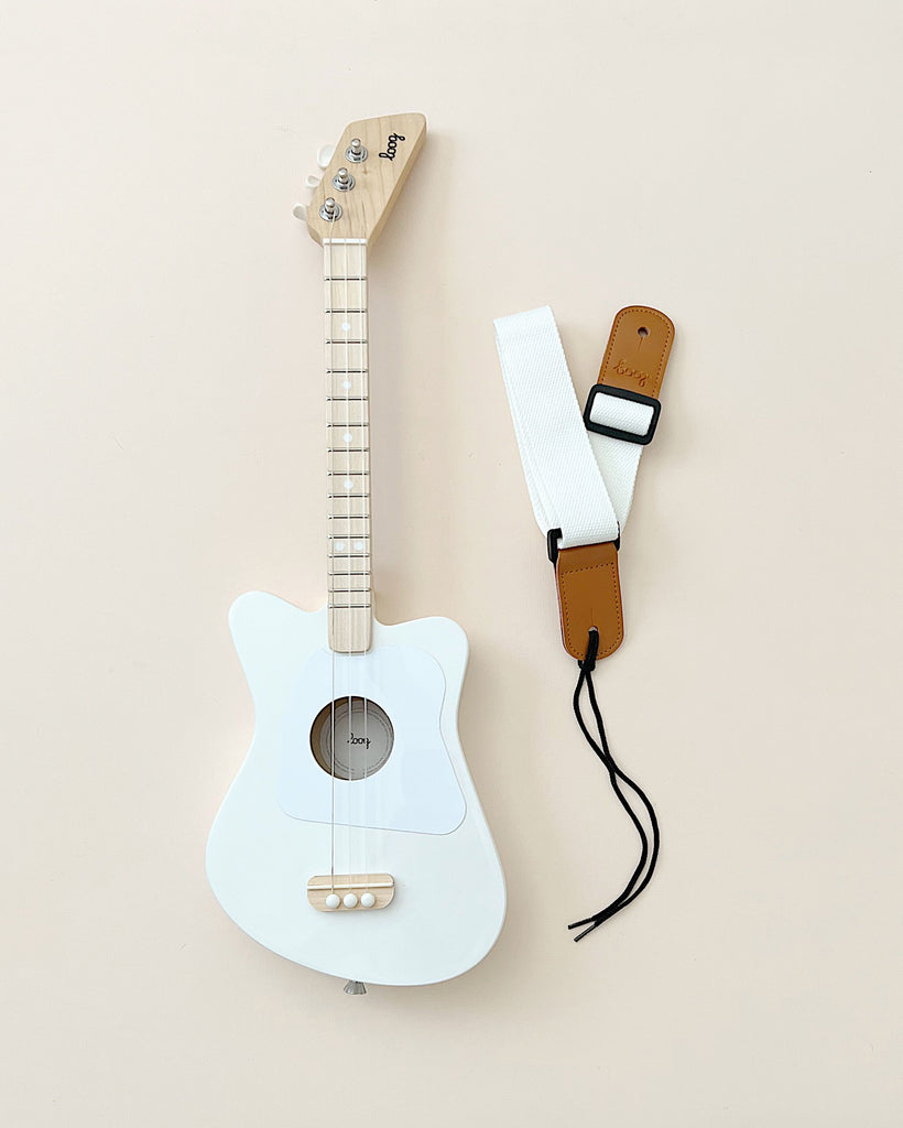 A wooden kid's guitar painted in white, photographed with a strap.