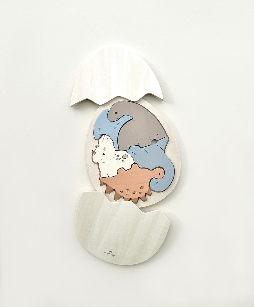 Wall art featuring a Dinosaur Egg Puzzle cracked open, with a cute depiction of baby dinosaurs hatching inside it, set against a plain white background.