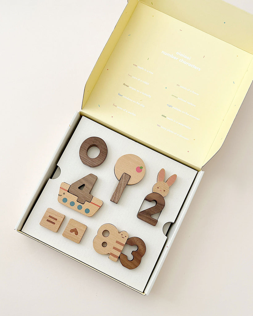 Open box with a Numbers Play Block Set collection of five wooden educational toys shaped like various animals and objects, like a rabbit and a boat, lying on a plain background. The box lid has text.