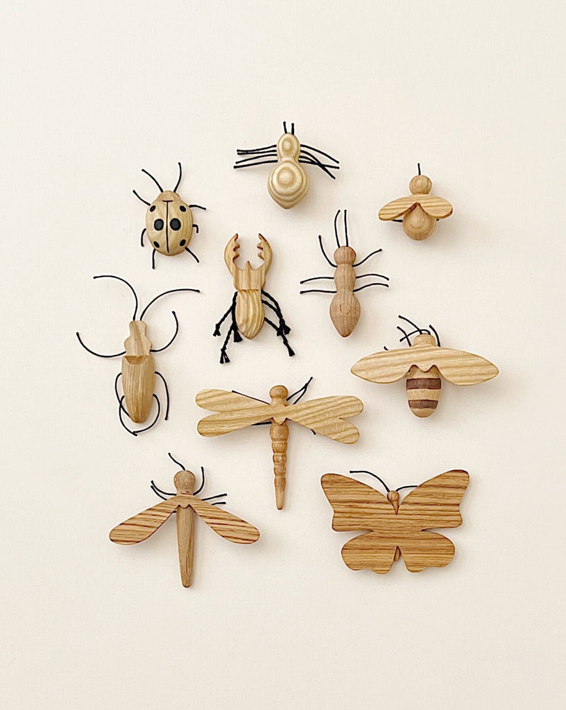 A collection of Handmade 11-Piece Wooden Insects, including a butterfly, dragonfly, beetle, and others, arranged neatly on a light background.